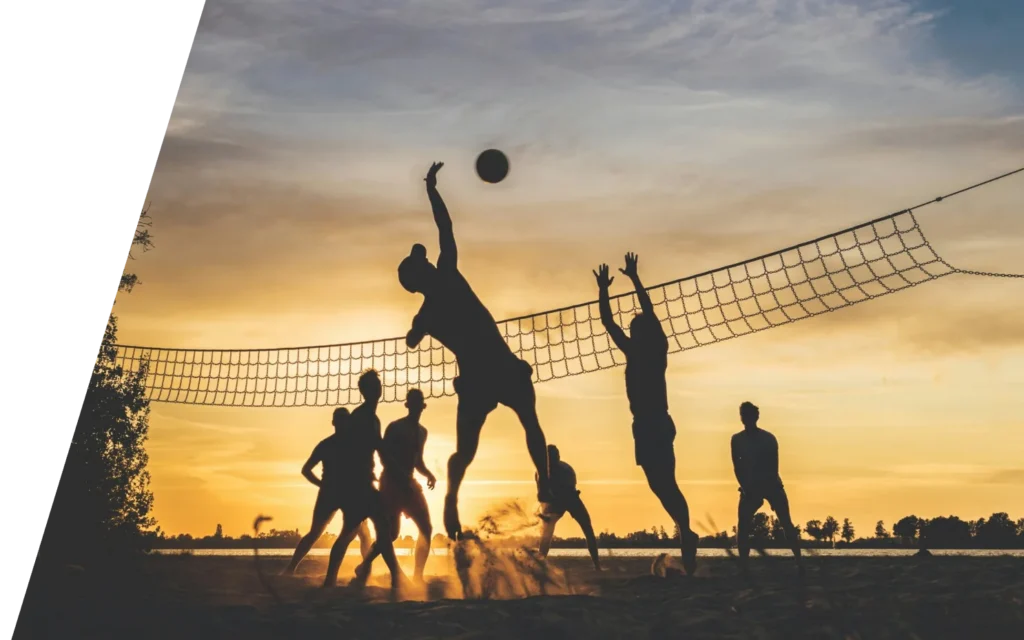 Beach volleyball players jumping at sunset, the kind of pivoting and jumping sport patients return to after revision ACL reconstruction